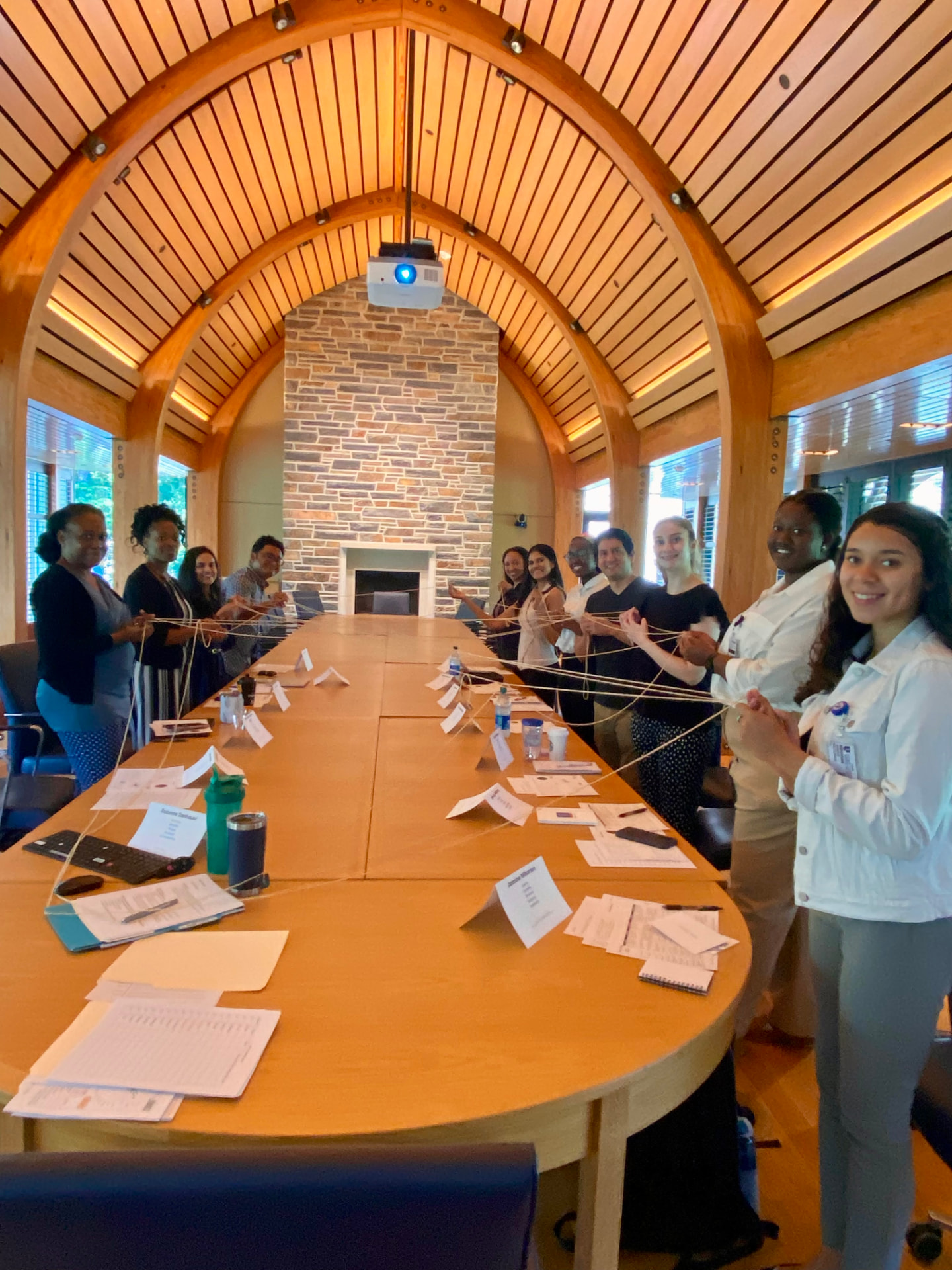 The REGAL team standing around a long wooden table during a retreat activity in a vaulted wooden room