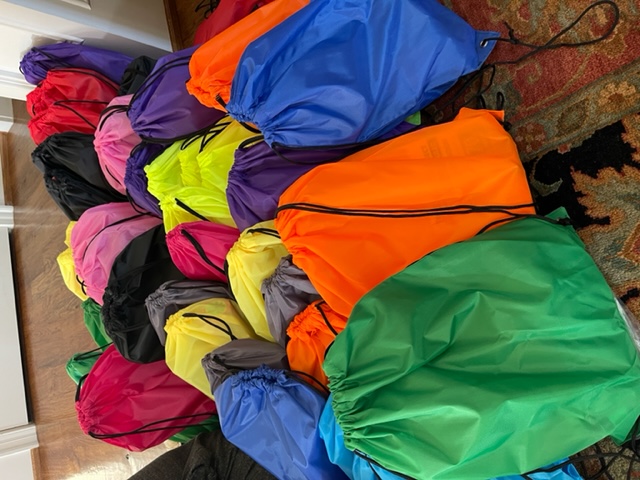 Dozens of brightly colored drawstring backpacks filled and ready for delivery