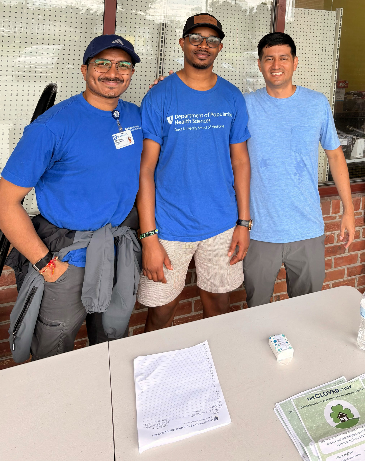 Three CLOVER study team members at an outdoor recruitment table with study flyers