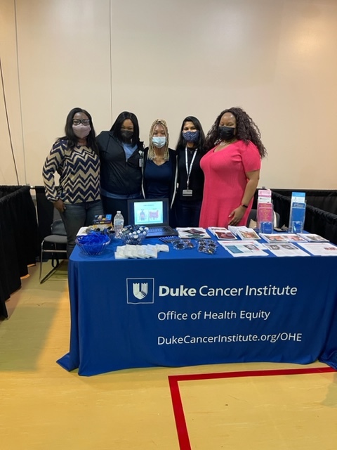Five team members behind a Duke Cancer Institute Office of Health Equity table at the Gut Patrol event