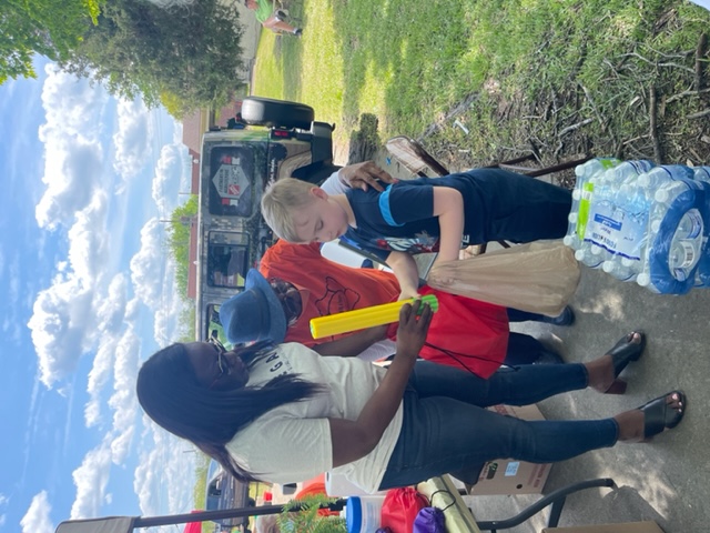 A team member handing supplies and water to a child at an outdoor community giveaway