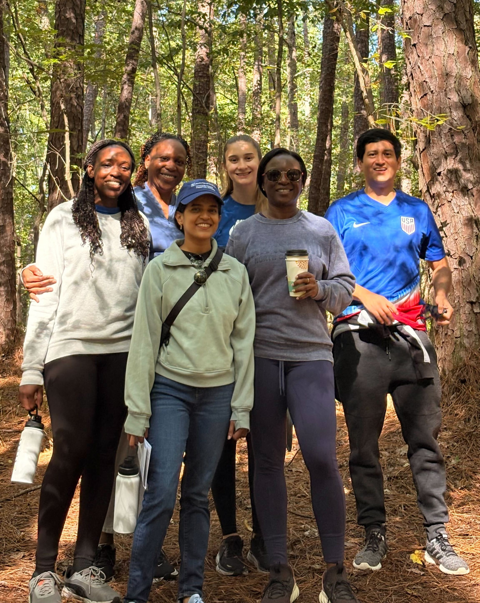 Six team members smiling on a wooded trail during a group hike at Umstead State Park