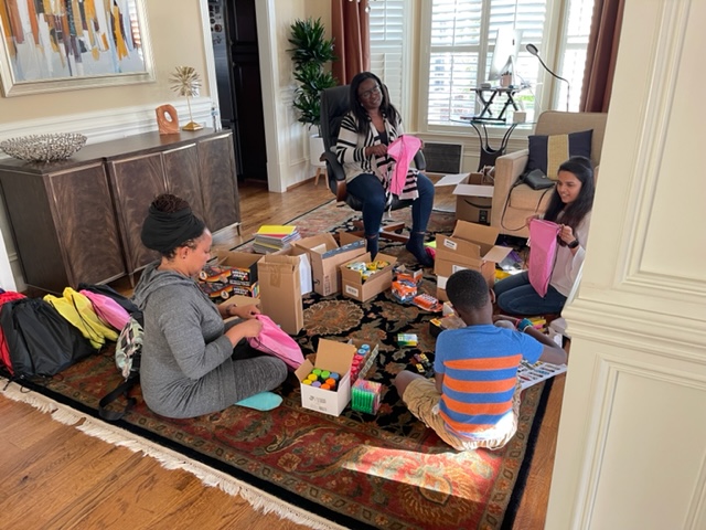 REGAL team members and family sorting school supplies and clothing into care packages on a living room floor